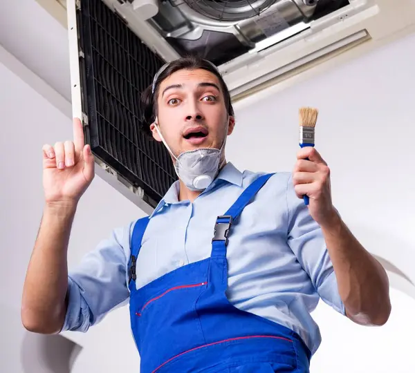 The young repairman repairing ceiling air conditioning unit