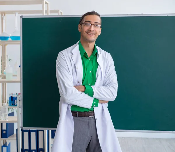 The young male chemist teacher in front of blackboard