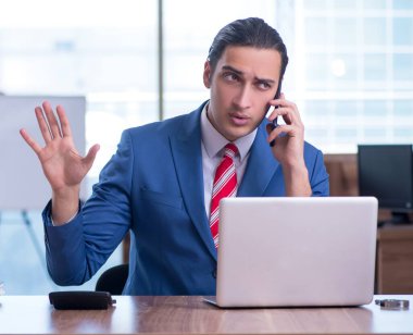 Genç yakışıklı işadamı ofiste oturuyor.