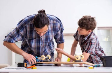 Genç baba oğluyla birlikte kaykay tamir ediyor.