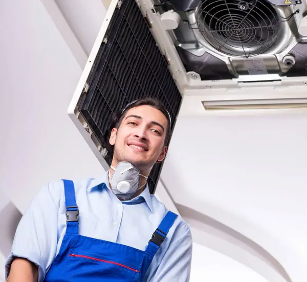 The young repairman repairing ceiling air conditioning unit