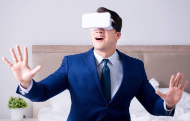 İş adamı yatak odasında sanal gerçeklik kulaklığı takıyor.