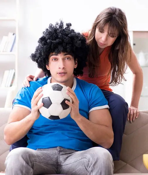 妻と一緒に家でサッカーを見ている若い男 ストック画像