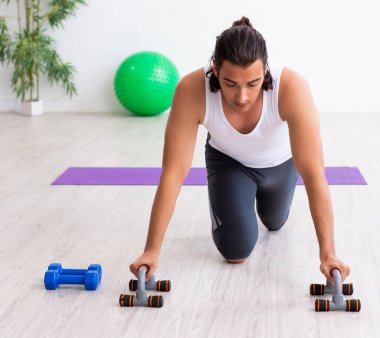 Genç yakışıklı adam içeride spor egzersizleri yapıyor.