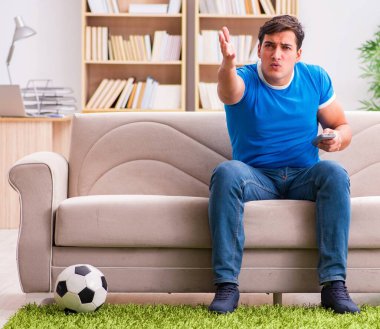 Evde kanepede oturup futbol izleyen adam.
