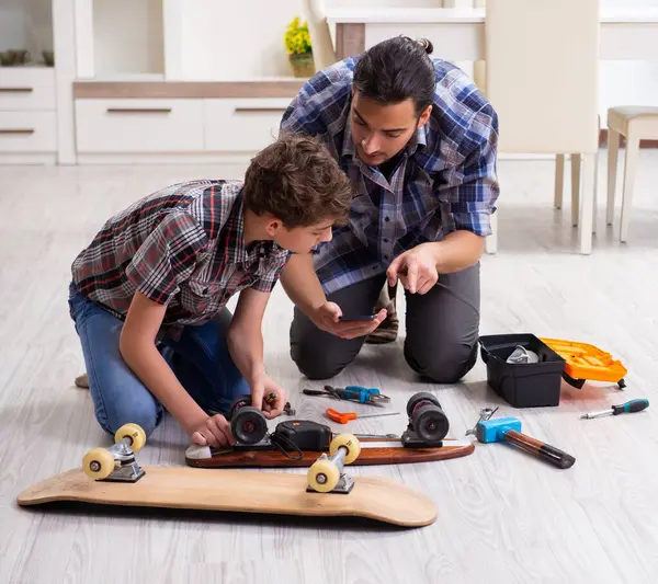 Genç baba oğluyla birlikte kaykay tamir ediyor.
