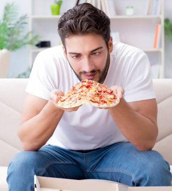 Pizza yiyen adam evde yemek yiyor, dinleniyor.