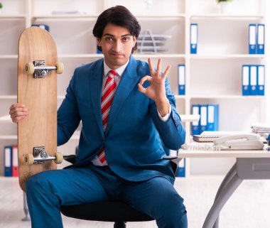 The young handsome businessman with longboard in the office clipart