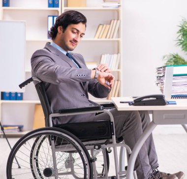 The young handsome employee in wheelchair at the office