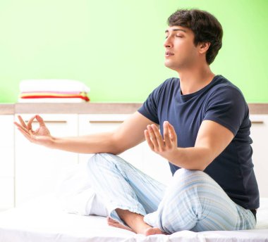 Pijamalı genç adam sabah egzersizi yapıyor.