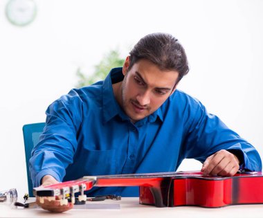 Genç erkek tamirci gitarı tamir ediyor.