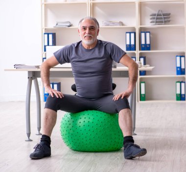 The white bearded old man employee doing exercises in the office