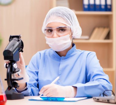 Mikroskop ve tüplerle çalışan laboratuvar kimyageri.