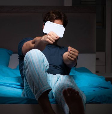 Genç adam gece yatağında bilgisayar oyunları oynuyor.