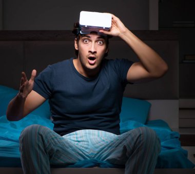 Genç adam gece yatağında bilgisayar oyunları oynuyor.