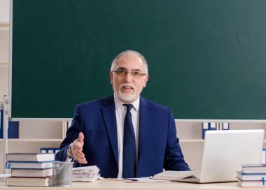 Tahtanın önündeki yaşlı erkek öğretmen.