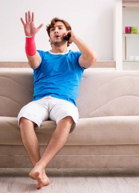 Kolu yaralı genç adam kanepede oturuyor.