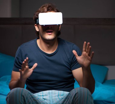 Genç adam gece yatağında bilgisayar oyunları oynuyor.