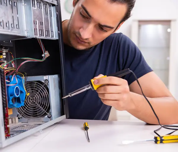 Genç adam evdeki bilgisayarı tamir ediyor.