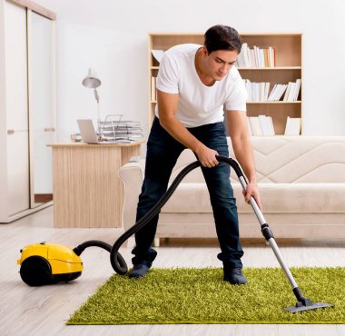 Evi elektrikli süpürgeyle temizleyen adam.