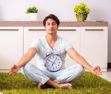Yatak odasında yoga yapan genç adam zaman yönetimi konseptinde.