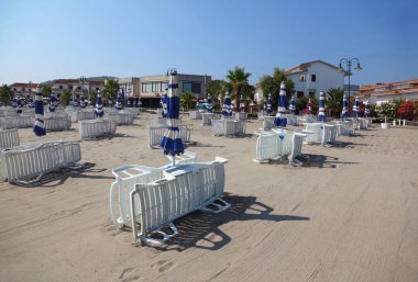 birçok beyaz çizgili şezlonglar ve boş sahilde plaj şemsiyeleri vardır. 