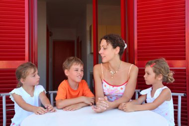 Three children and mother sit on  verandah  round table near doors and speak clipart