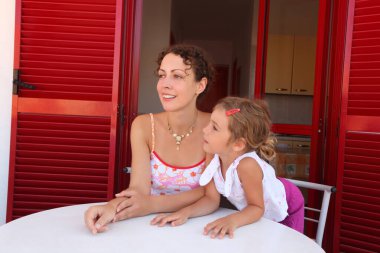 Kız ve anne kapının yanındaki verandada oturur ve yan bakarlar.