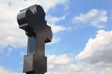 Mezarlıkta siyah granit haç, bulutlu mavi gökyüzü