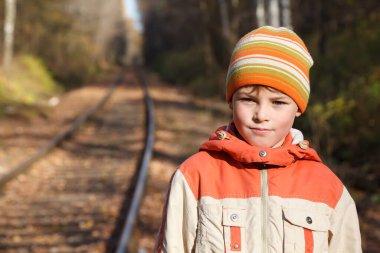 Demiryolundaki sonbahar güneşli erkek çocuğunun portresi. Ceketi ve şapkası var..