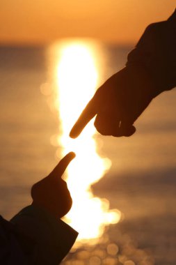 Gün batımına yakın iki el çocuk ve anne parmaklarına dokunuyor.