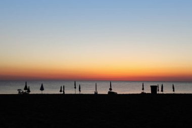 Gün batımında kumsalda kapalı şemsiyeler ve şezlonglar.