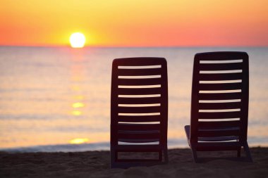 Akşamları sahilde, deniz günbatımını izleyen iki boş lacivert sandalye.