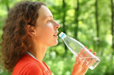 Kadın şişeden su içiyor ve önüne bakıyor.