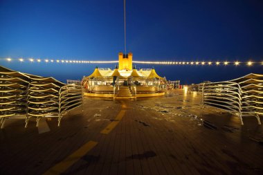 Akşamları yolcu gemisinin aydınlatılmış güvertesi. resim merkezinde bar ve tablolar.