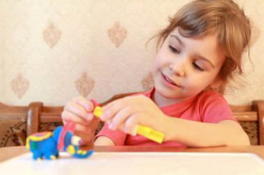 Küçük kız masada ve plastikçiden modeller, kıza odaklan.