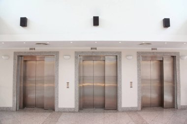 Ofis binasında krom kaplamalı üç asansör.