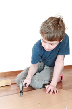 Küçük çocuk yerde oturuyor ve çekiçle tahtaya çivi çakıyor.