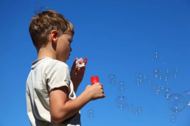 Oğlan yan duruyor ve sabun köpüklerini şişiriyor.