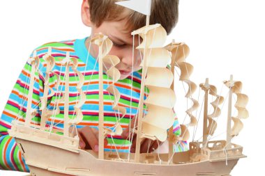 Small boy in striped shirt work with zeal on hull of artificial ship, focus on boat clipart