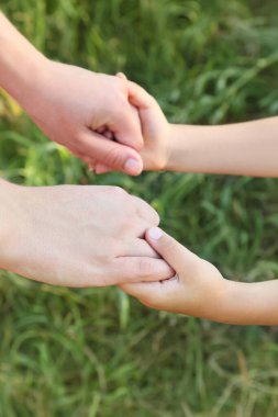 Anne ve oğulun ellerinin birbirine yakın duruşu, yeşil çimenler, dikey, sığ odak derinliği