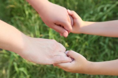 Anne ve oğulun ellerinin birbirine yakın duruşu, yeşil çimenler, yatay