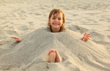 Yüzdükten sonra küçük kız kumsalda gömülür, bir sürü sarı kum.