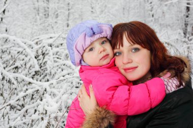 Genç, güzel anne, küçük kızı kışın karda ormanda kucaklıyor.