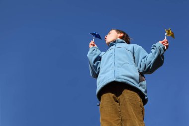 Mavi ceketli ve kahverengi pantolonlu küçük çocuk ellerinde fırıldak gibi uçuyor.