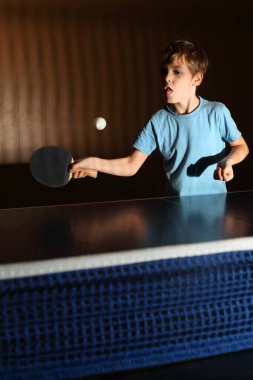 Ping pong oynayan küçük çocuk; konsantre yüz; çocuk dilini dışarı çıkardı