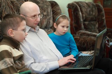 Father, son and daughter sitting on couch and look at laptop screen, serious faces, focus on boy clipart