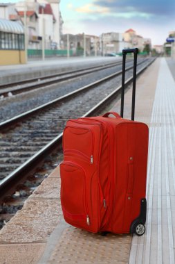 Büyük kırmızı seyahat çantası tren raylarının yanındaki platformda duruyor. perspektif