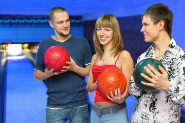 İki erkek bovling topunu tutuyor ve ortada duran kıza bakıyor, soldaki kıza ve ortadaki kıza odaklanıyor.