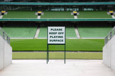 Rows of folded, green, plastic seats in very big, empty stadium, warning inscription clipart